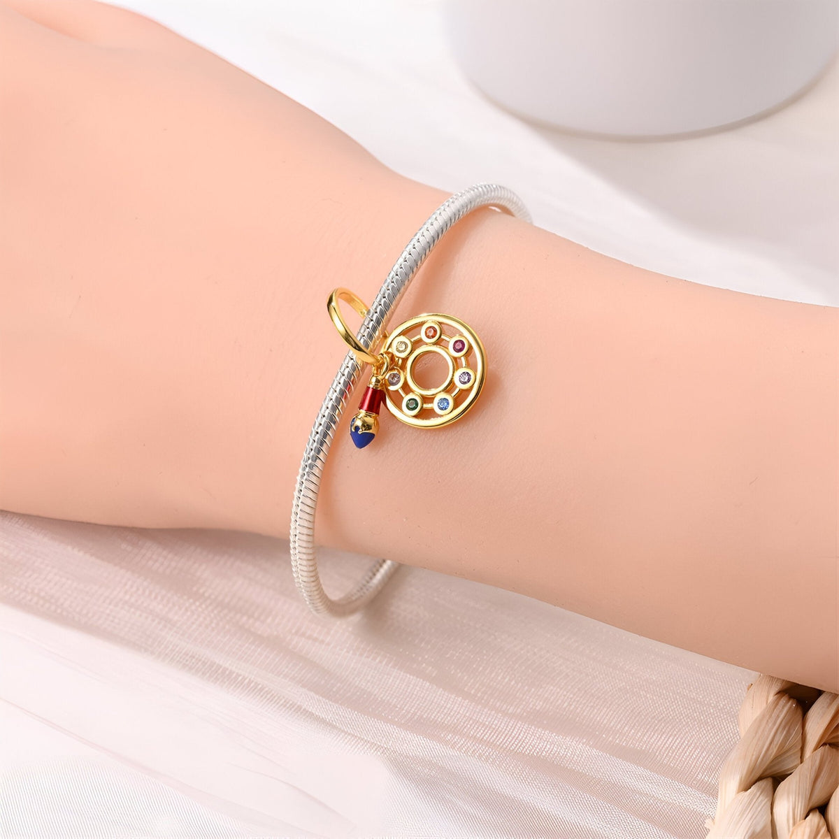 Bracelet argenté fin avec pendentif pinceau doré orné de pierres colorées scintillantes.