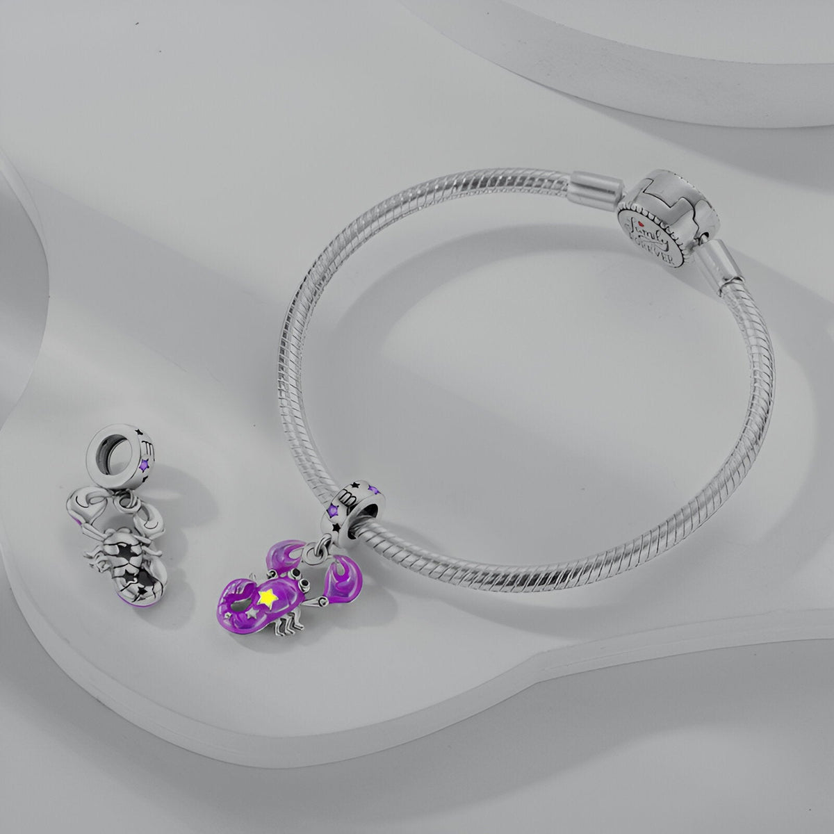 Bracelet argenté avec pendant charme signe Balance violet et deux breloques argentées supplémentaires.