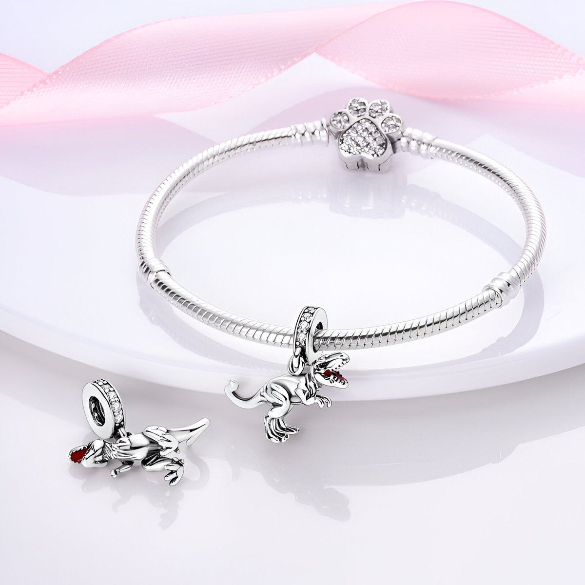 Bracelet argent avec pendentif T-Rex détaillé et fermoir en forme de fleur sur fond rose pâle.