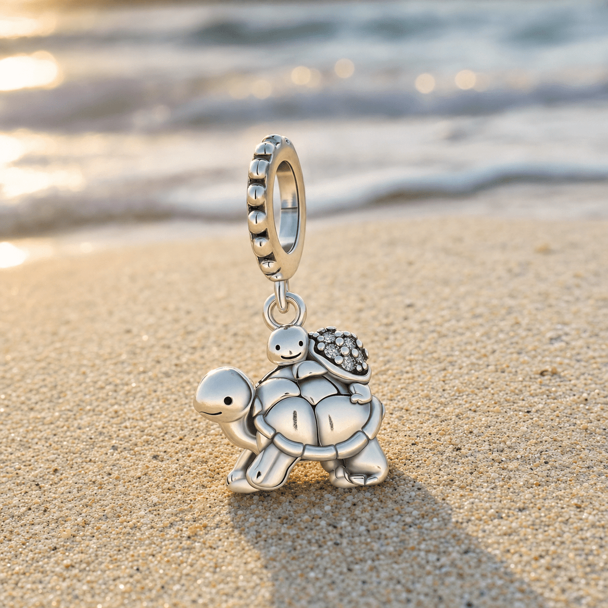 Charm tortues mère et enfant en argent posé sur le sable d'une plage au coucher du soleil