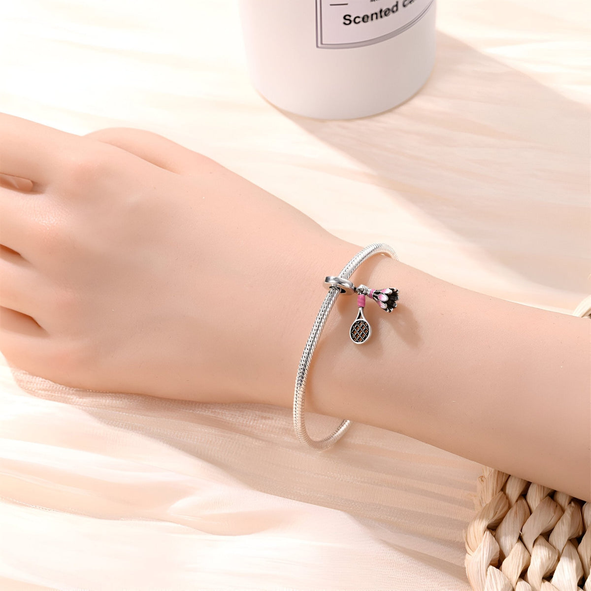 Bracelet argenté avec pendentifs volant de badminton et raquette, porté au poignet féminin.