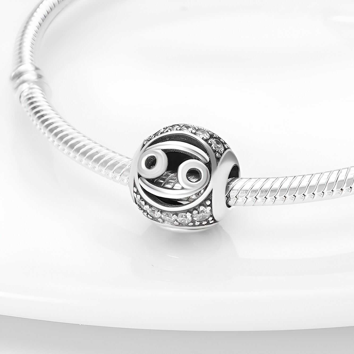 Charm rond argenté signe zodiaque Poisson avec détails blancs et strass sur bracelet serpent en acier lumineux.
