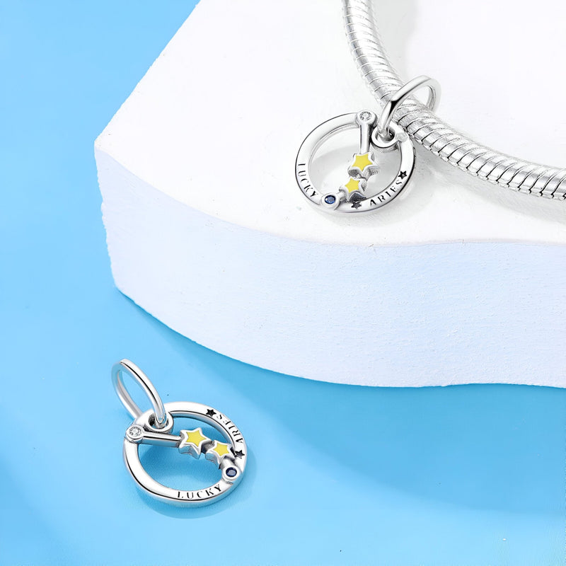 Charm en argent avec signe bélier, étoile jaune et pierres bleues sur cercle gravé.