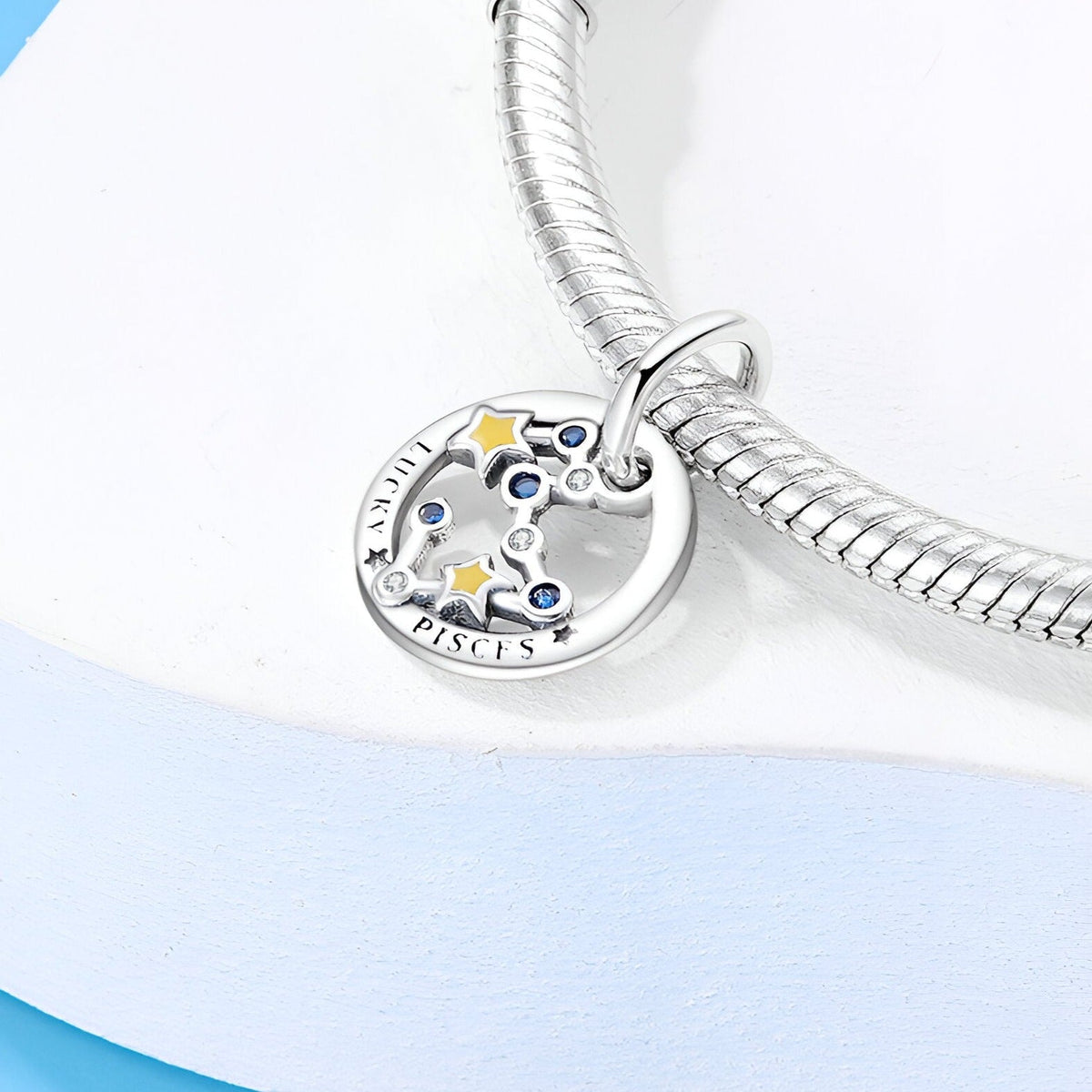 Charm rond en argent avec étoiles colorées et inscription "Pisces" sur bracelet serpent en métal argenté.