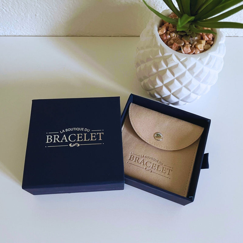 Coffret bleu foncé avec intérieur beige contenant un bracelet fin avec petit pendentif doré.