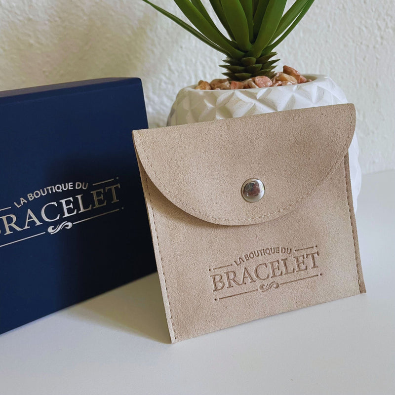 Pochette beige en toile avec bouton pression et logo La Boutique du Bracelet, boîte bleue en arrière-plan.