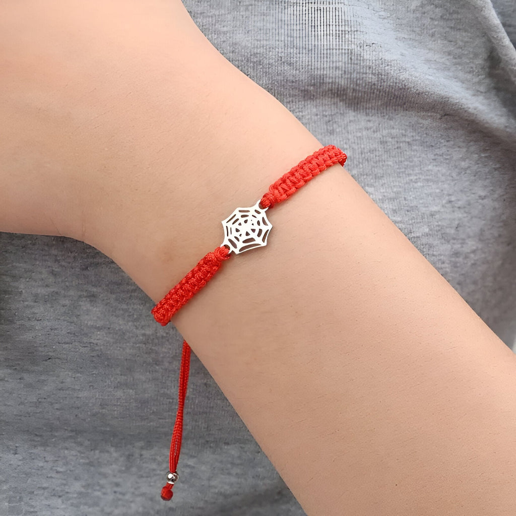 Bracelet cordon rouge avec pendentif araignée en acier argenté sur poignet clair.