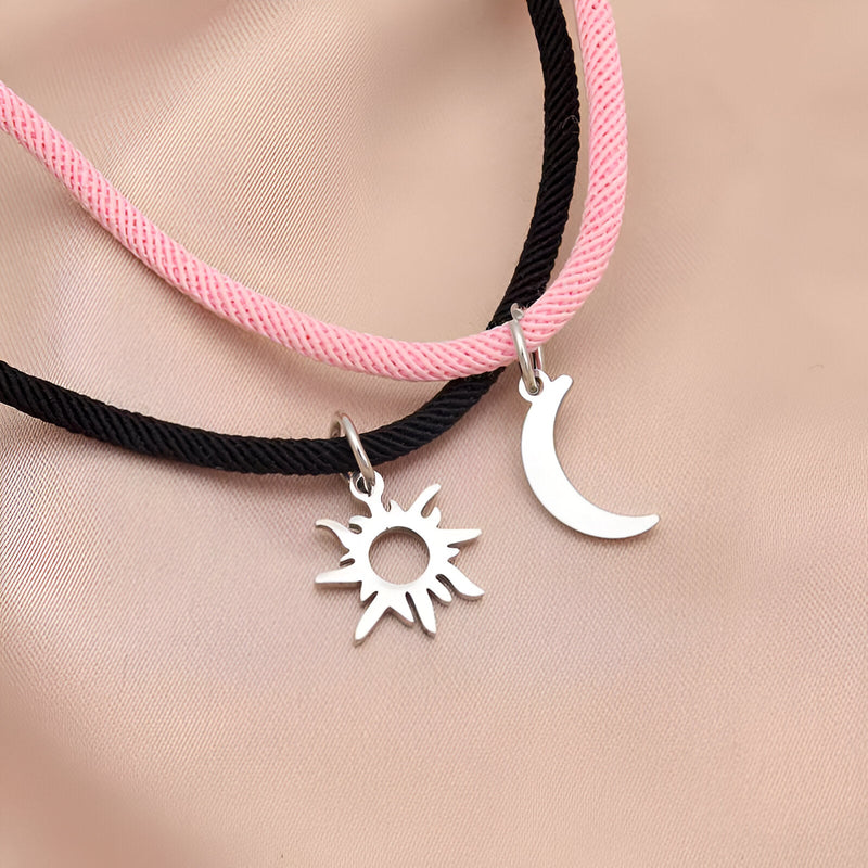 Duo de bracelets cordon rose et noir avec pendentifs soleil et lune argentés.
