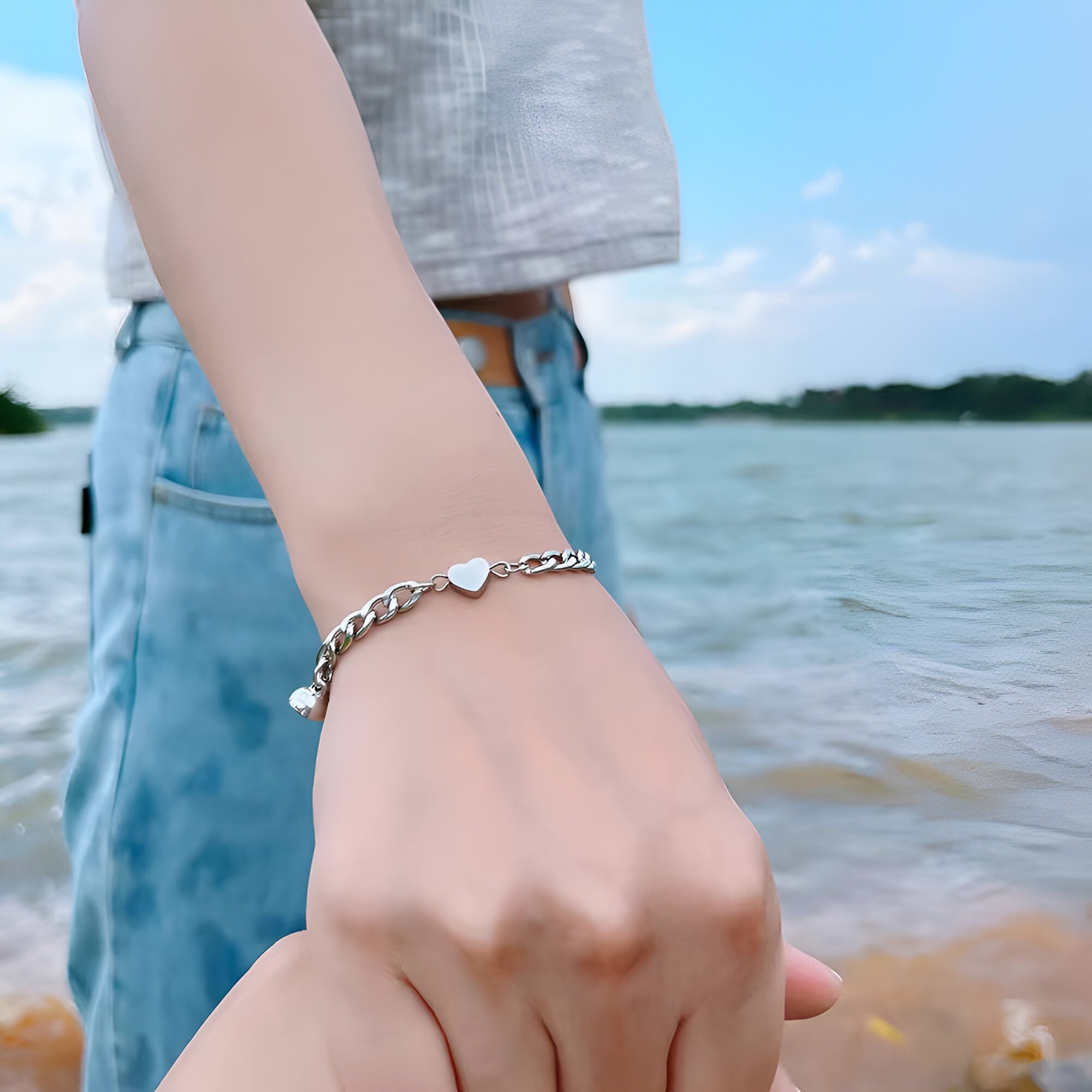 Duo de bracelets en acier inoxydable argenté avec pendentifs cœurs, porté sur poignet face à un lac.