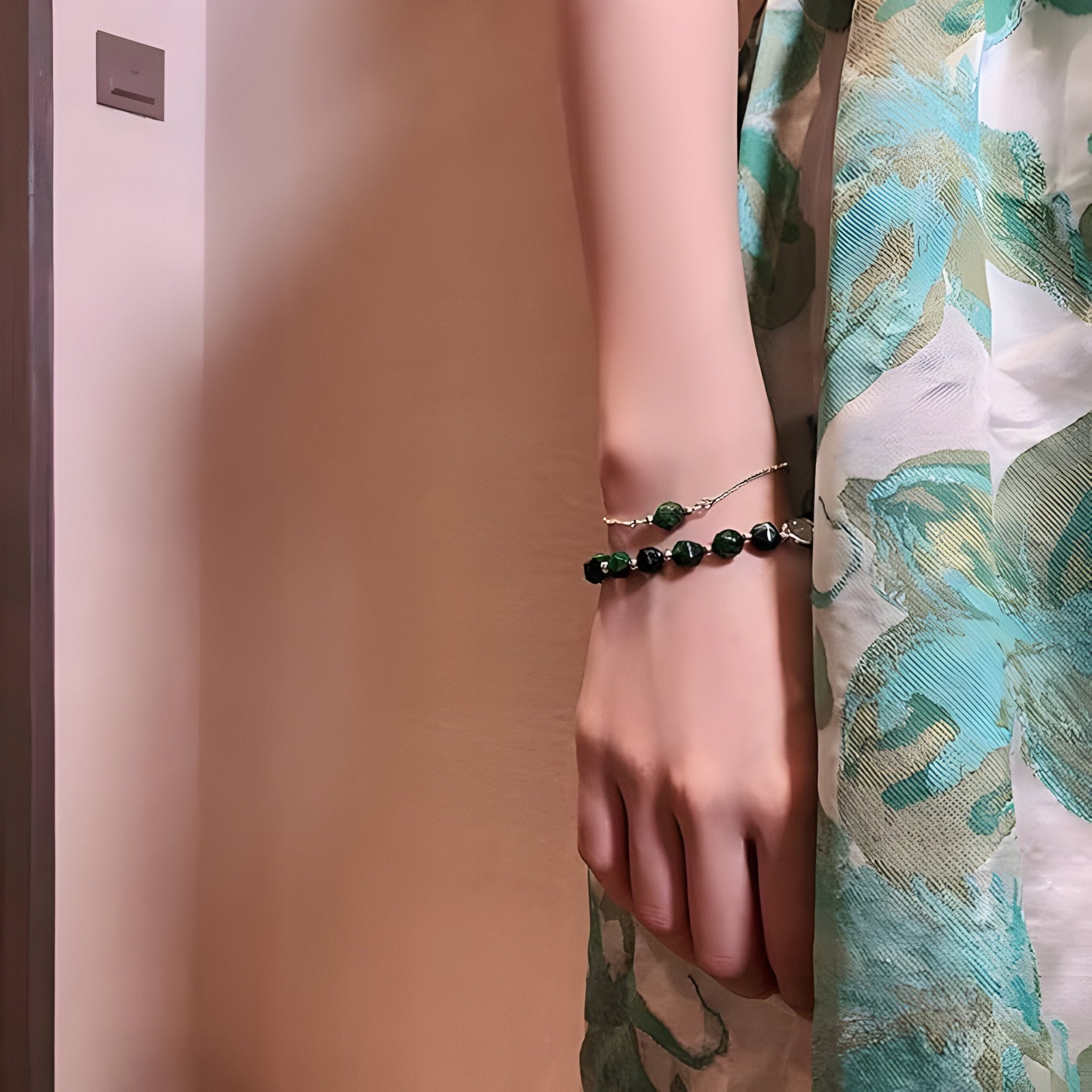 Duo de bracelets en perles d'œil de tigre vert scintillant sur poignet féminin, porté avec robe fleurie verte et beige.