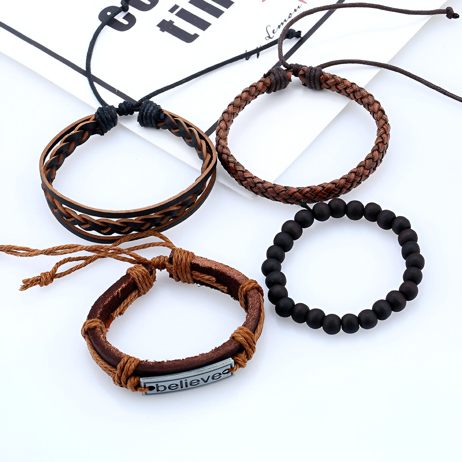 Ensemble de 4 bracelets marron avec cordons, perles noires, et plaque "believe" en métal.