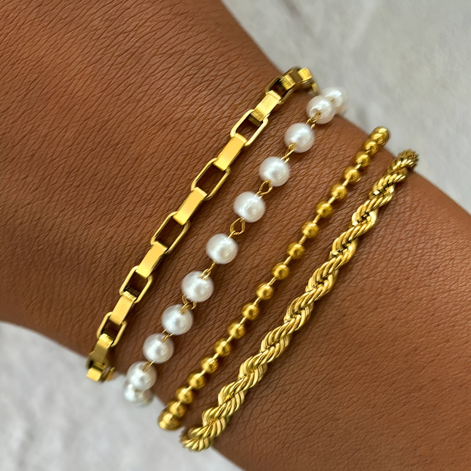 Quatre bracelets femme en acier inoxydable doré, incluant chaine plate, perles, billes, et torsadé.