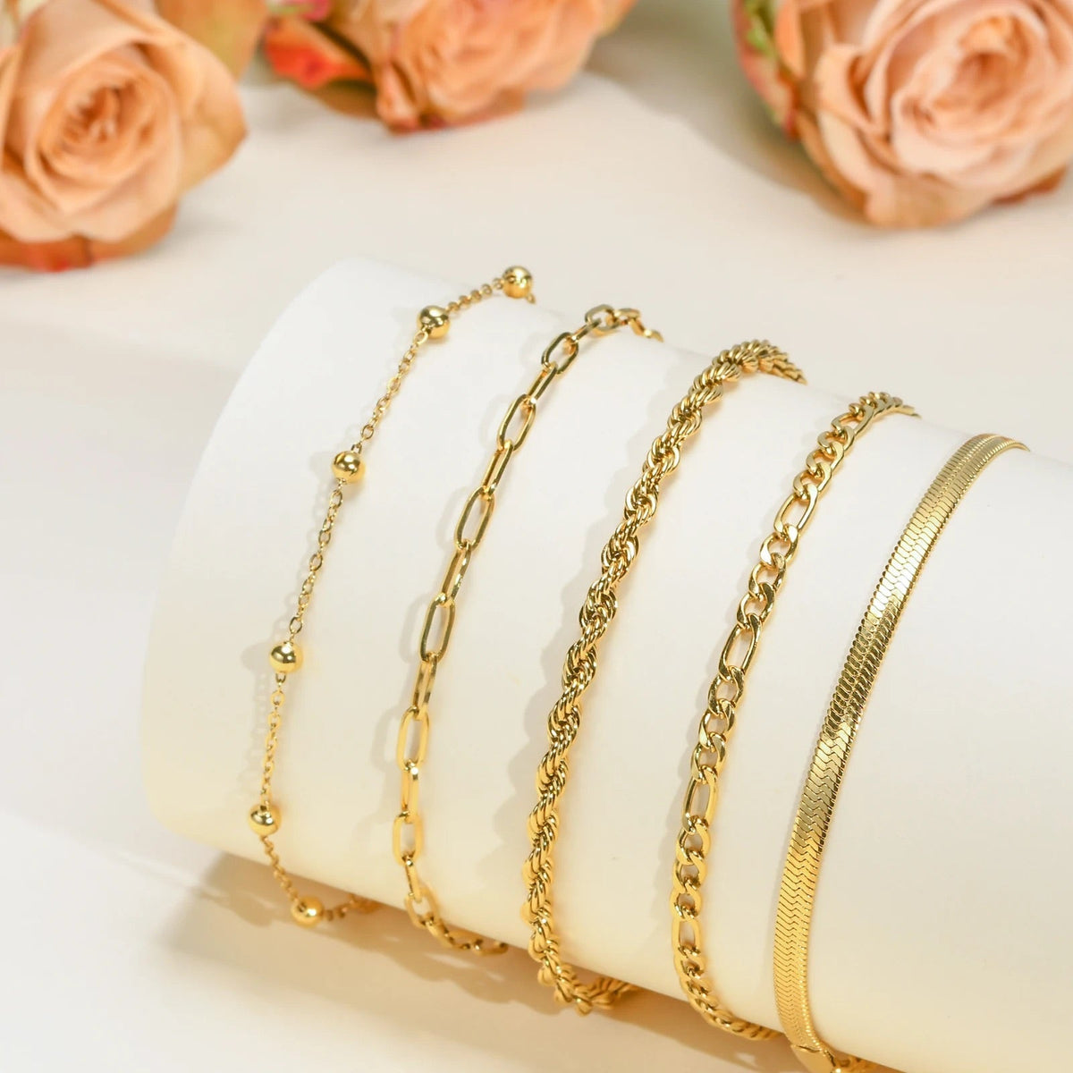 Ensemble de 5 bracelets fins en acier inoxydable doré aux mailles variées, du plus délicat au plus épais, présenté sur un.