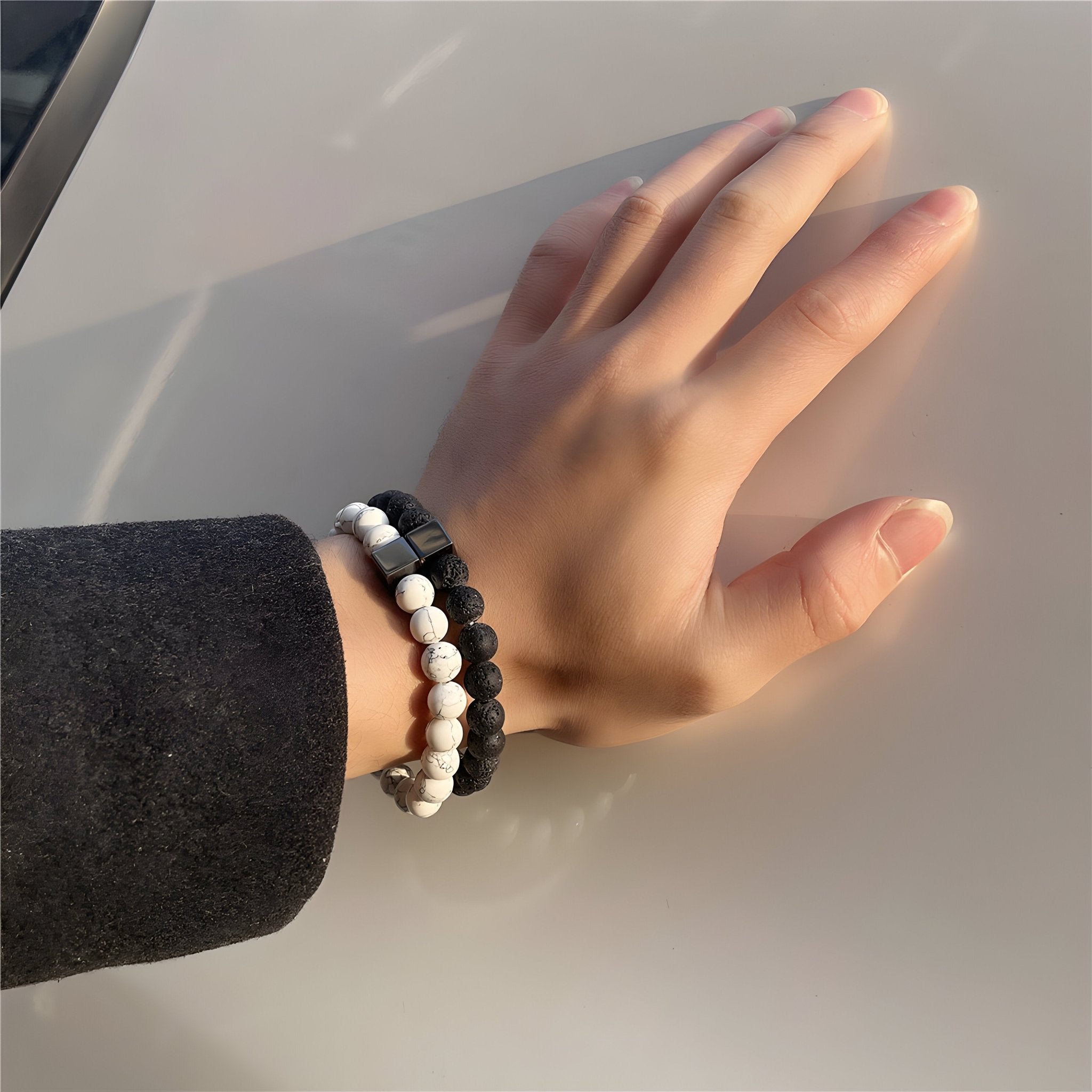 Paire de bracelets élastiques en pierres volcaniques noires et blanches portés au poignet homme.