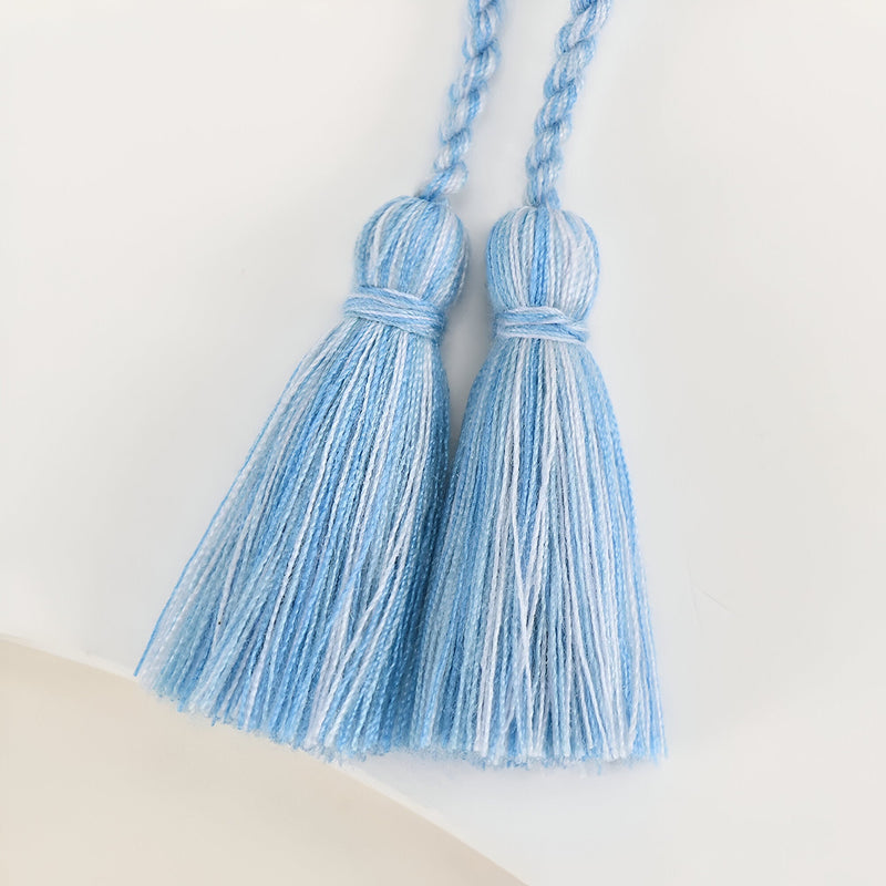 Paire de pompons en fil bleu clair avec tissage détaillé et boucle tressée.