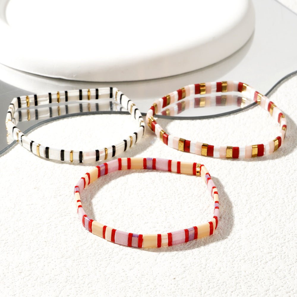 Trio de bracelets en perles japonaises multicolores avec motifs rayés blanc, rouge, noir et or.