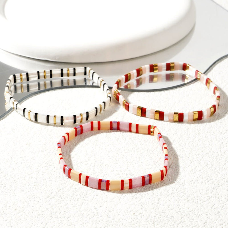 Trio de bracelets en perles japonaises multicolores avec motifs rayés blanc, rouge, noir et or.