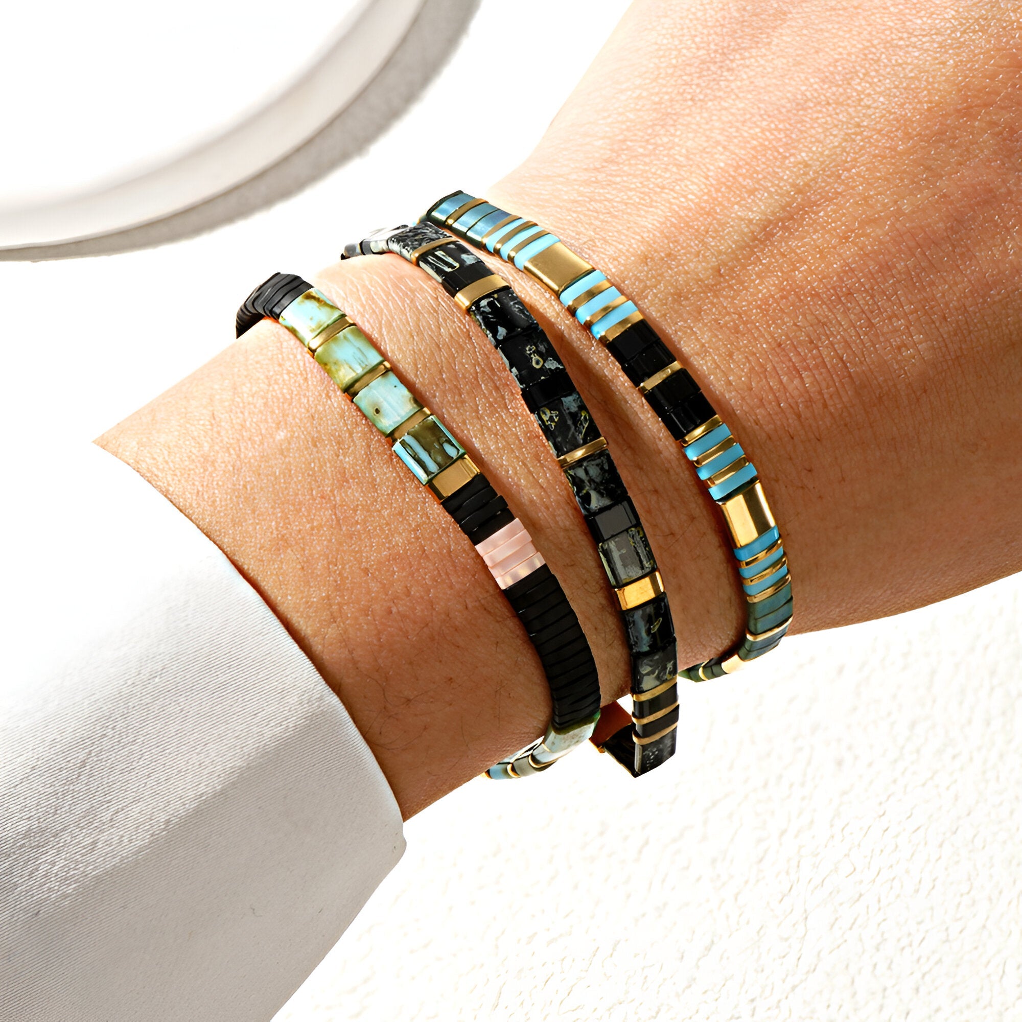 Trio de bracelets fins en perles turquoise, noires et or sur poignet féminin.
