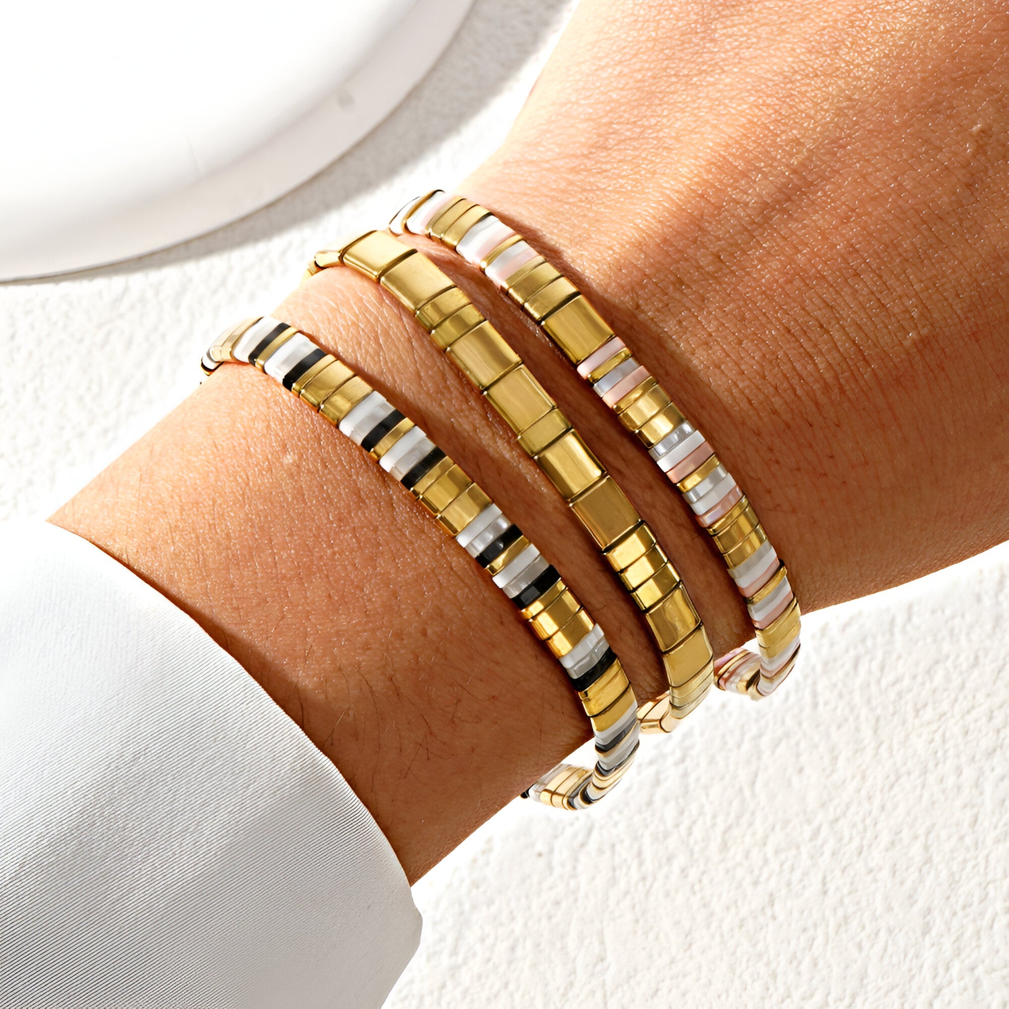 Trio de bracelets en perles dorées et carrées style Japonais, porté au poignet féminin.