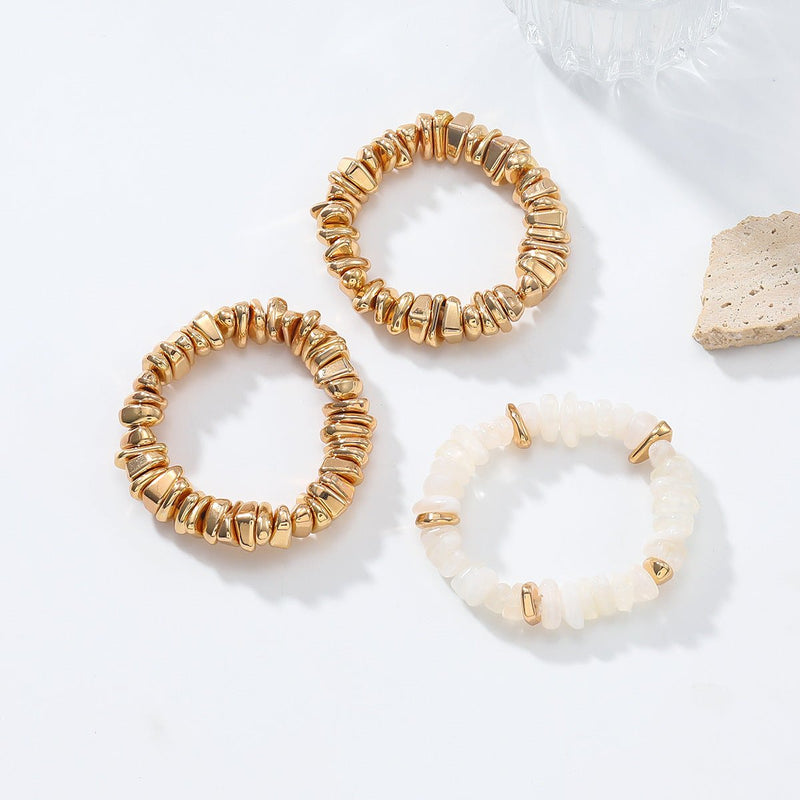 Trio de bracelets femme esprit soirée, deux dorés en perles métalliques rondes, un blanc nacré avec accents dorés.