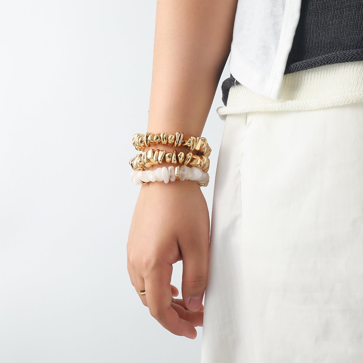 Trio de bracelets dorés et blancs, style chic et texturé, portés au poignet féminin.
