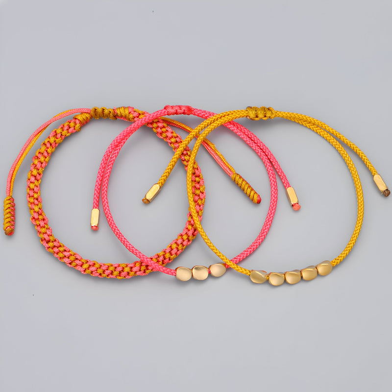 Trio de bracelets tibétains en corde rose, rouge et jaune avec perles en cuivre doré.