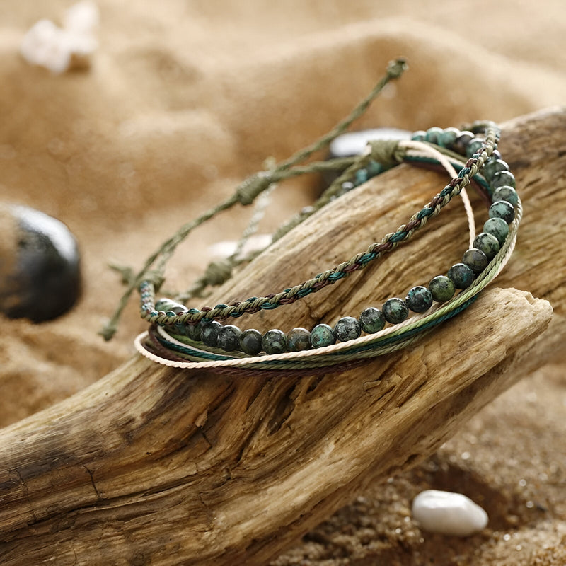 Trio de bracelets tibétains en pierre naturelle verte et fil ciré vert foncé sur bois flotté.