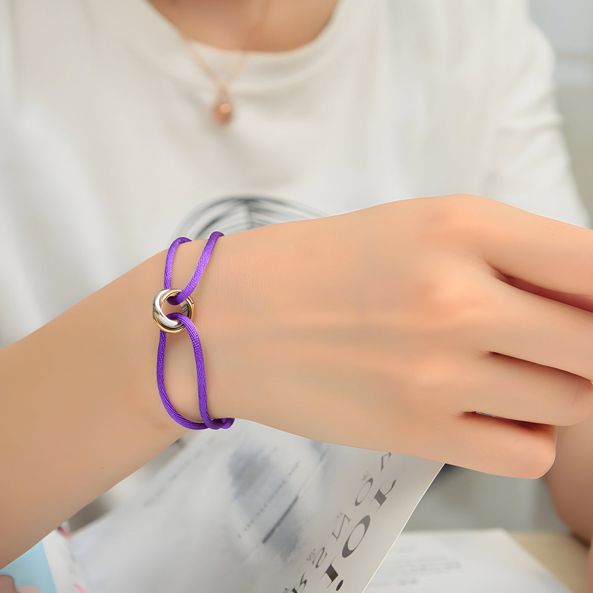 Bracelet cordon violet avec cercles entrelacés en métal argenté sur poignet féminin.