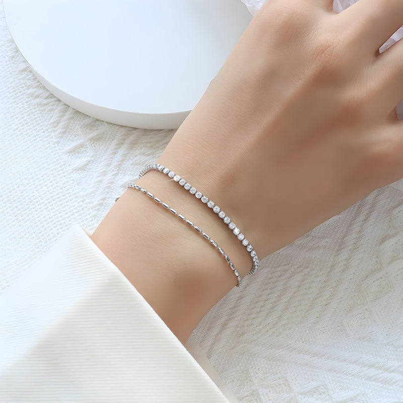 Bracelet double chaîne en titane argenté avec rangée de petites pierres claires, porté au poignet féminin.