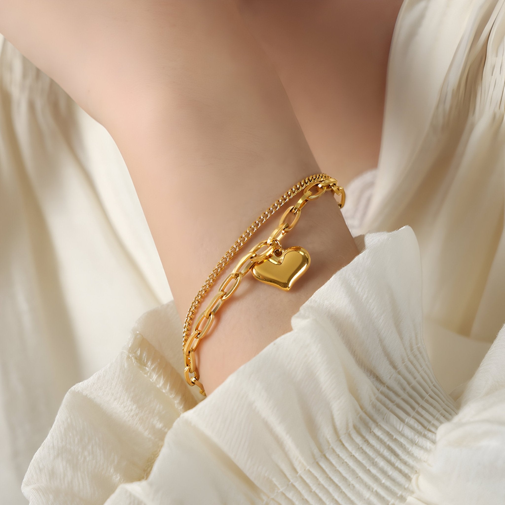 Bracelet double en titane plaqué or avec pendentif cœur lisse sur poignet féminin beige clair.
