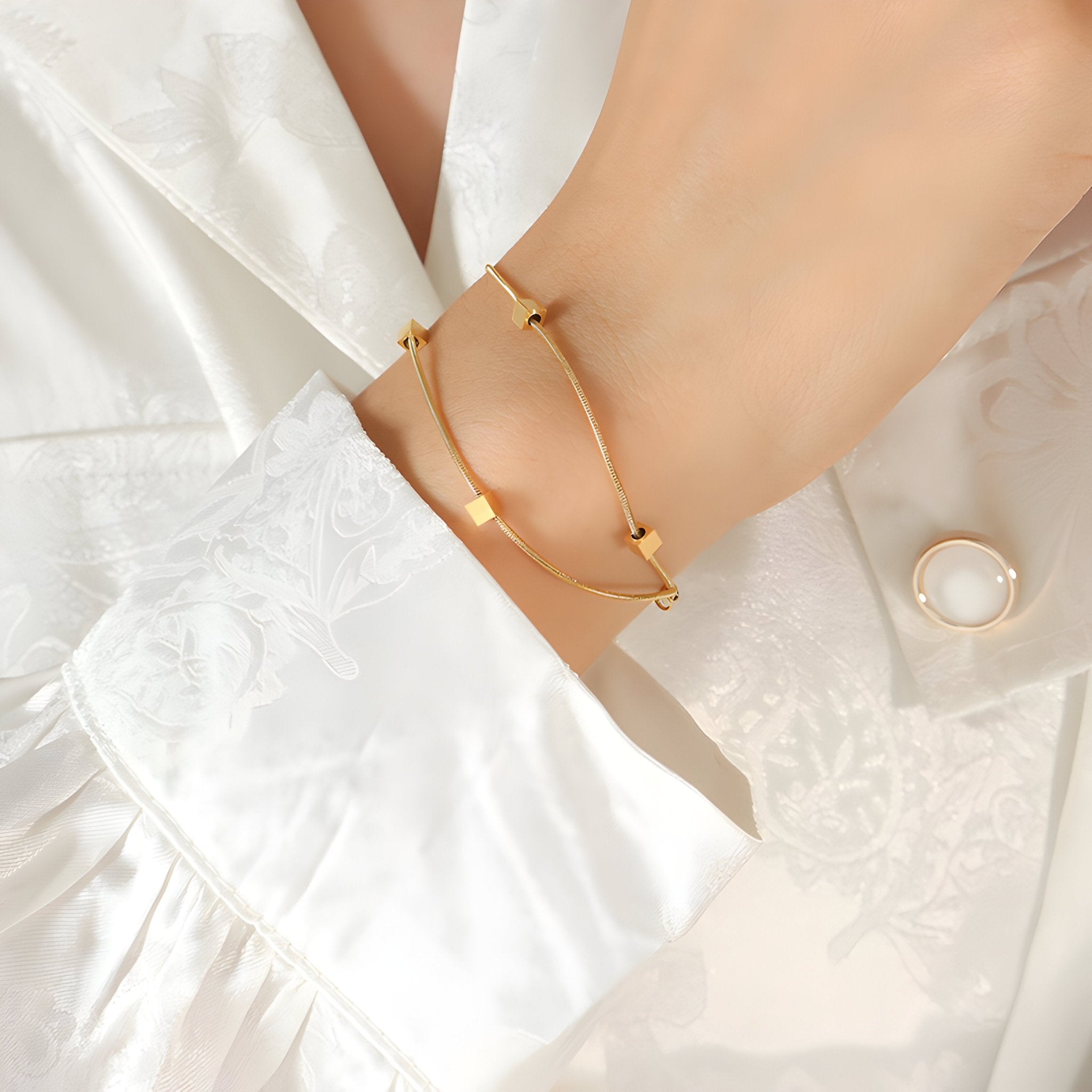 Bracelet double en titane plaqué or avec petits cubes géométriques élégants porté au poignet.