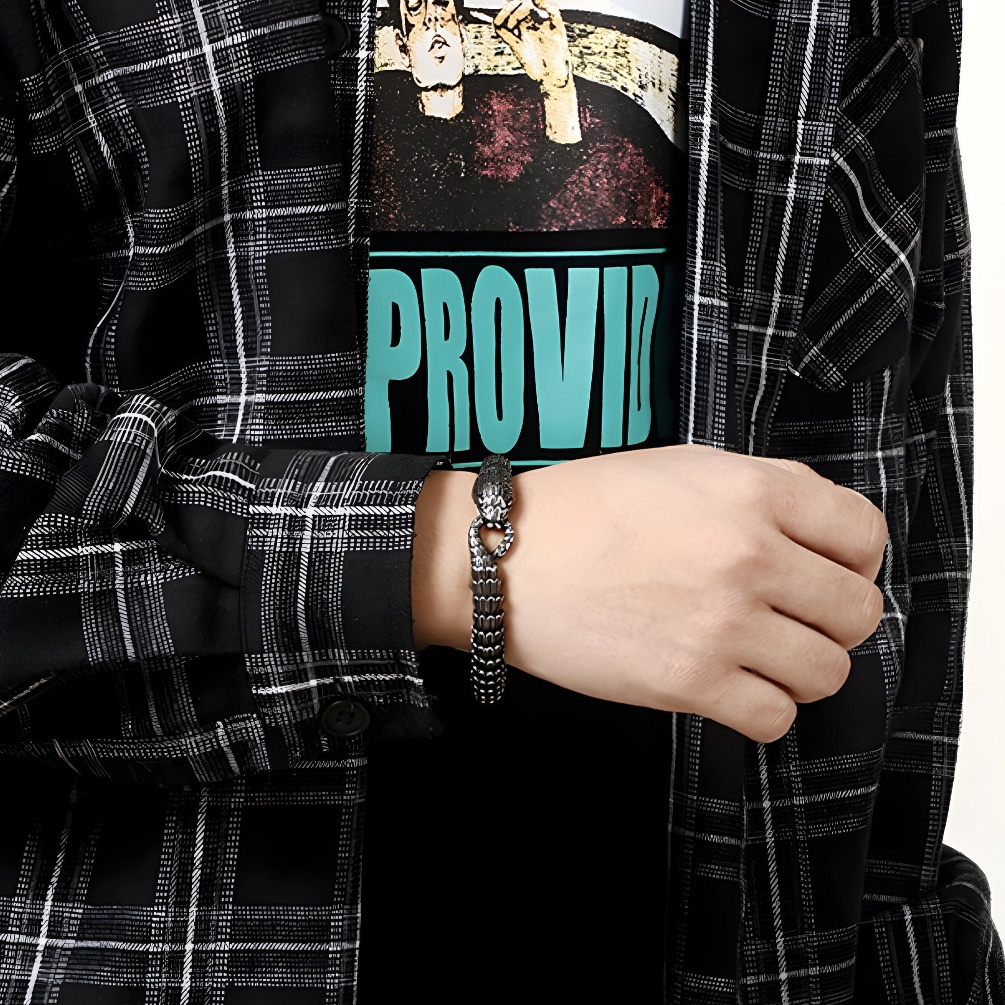 Bracelet serpent en acier inoxydable noir porté avec chemise à carreaux et t-shirt graphique bleu.