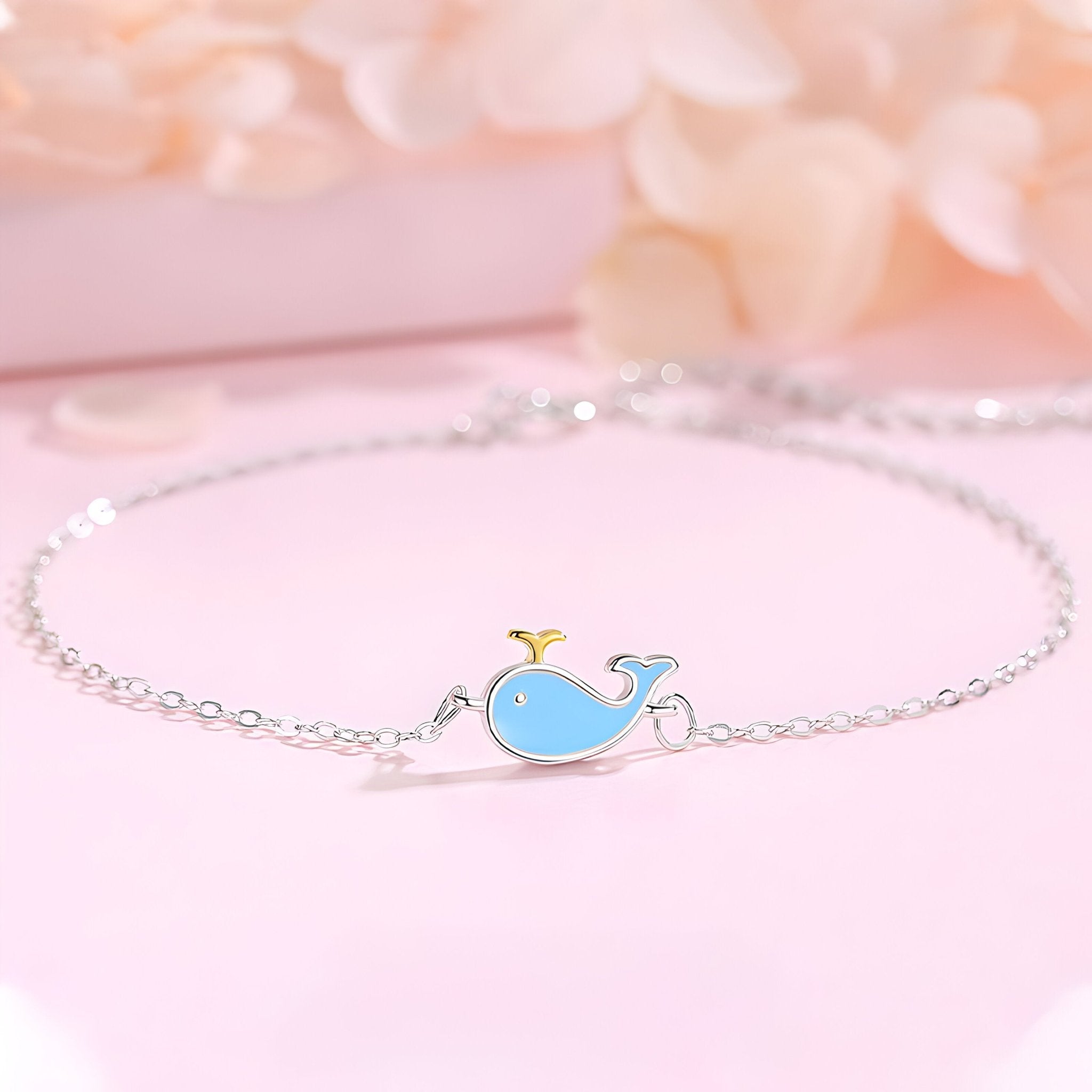 Bracelet fin en argent sterling avec pendentif baleine bleue émaillée sur fond rose pâle.