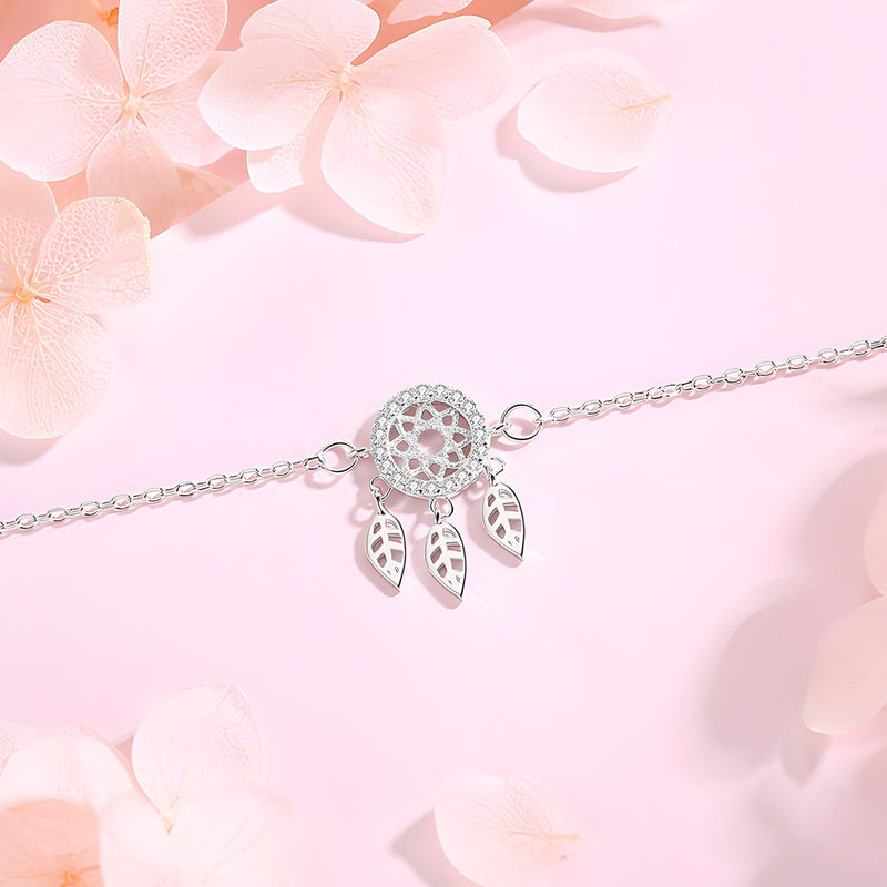 Bracelet en argent sterling avec pendentif attrape-rêves et trois plumes délicates sur fond rose pâle.