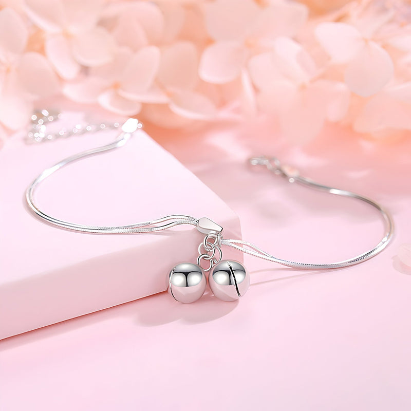 Bracelet fin en argent sterling avec deux perles sphériques suspendues sur fond rose pâle.