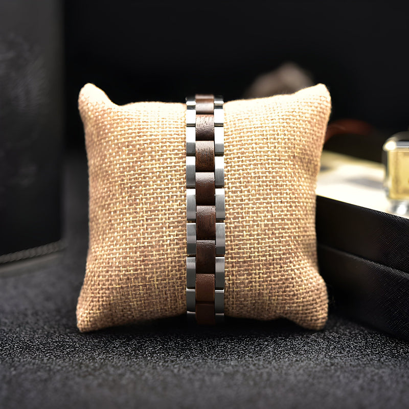 Bracelet pour homme en bois de noyer marron avec maillons argentés sur coussin en toile beige.