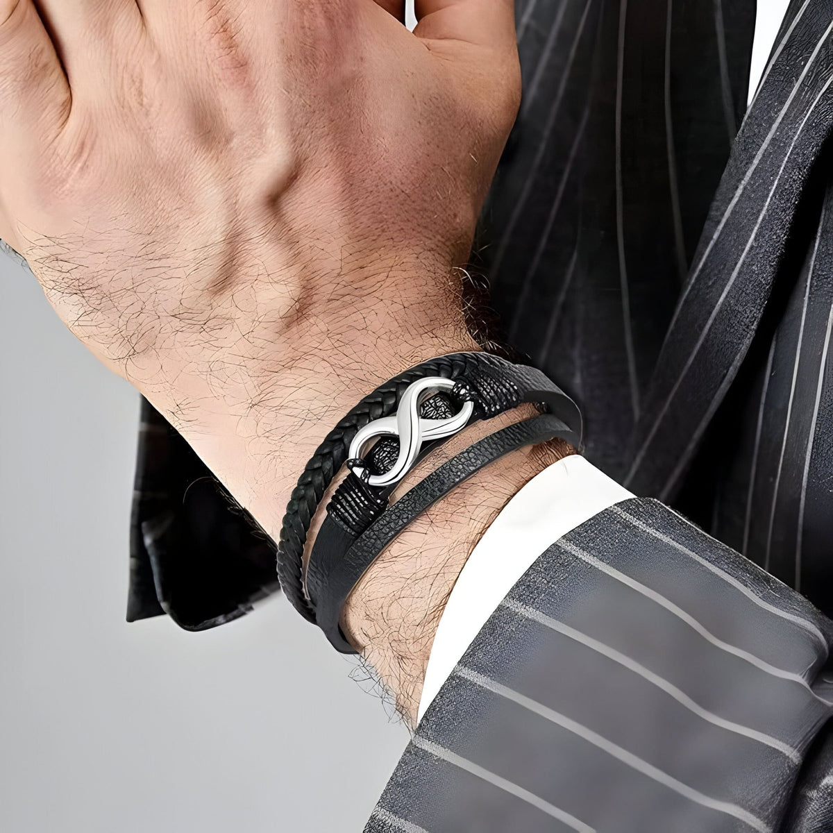 Bracelet multi-rangs en cuir noir avec motif infini en métal argenté porté au poignet.