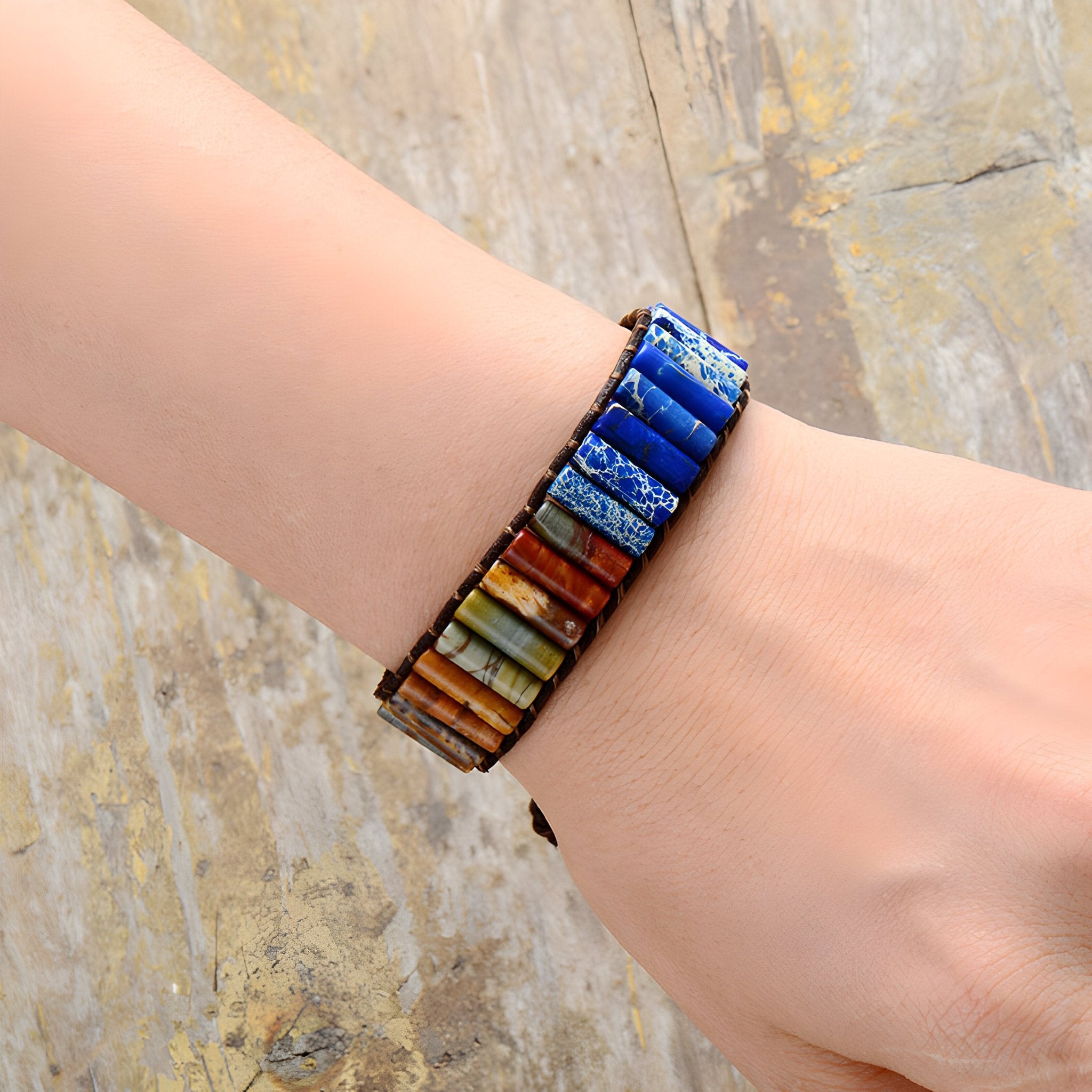 Bracelet multi-rangs en pierres de jaspe multicolores sur cuir marron porté au poignet féminin.