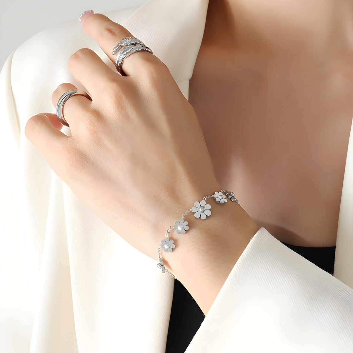Bracelet argenté en titane avec fleurs délicates, porté au poignet d'une femme en veste blanche.