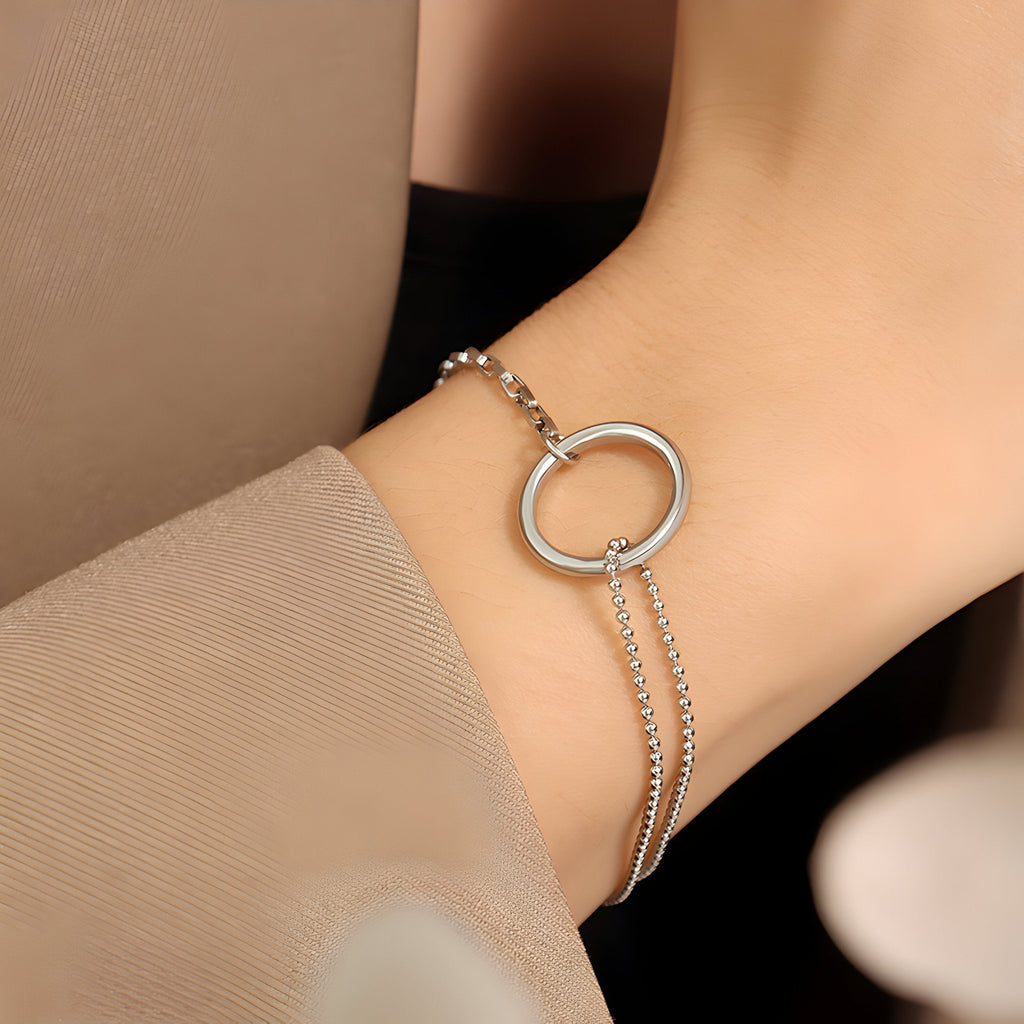 Bracelet en titane argenté avec double chaîne fine et anneau ovale central sur poignet femme.