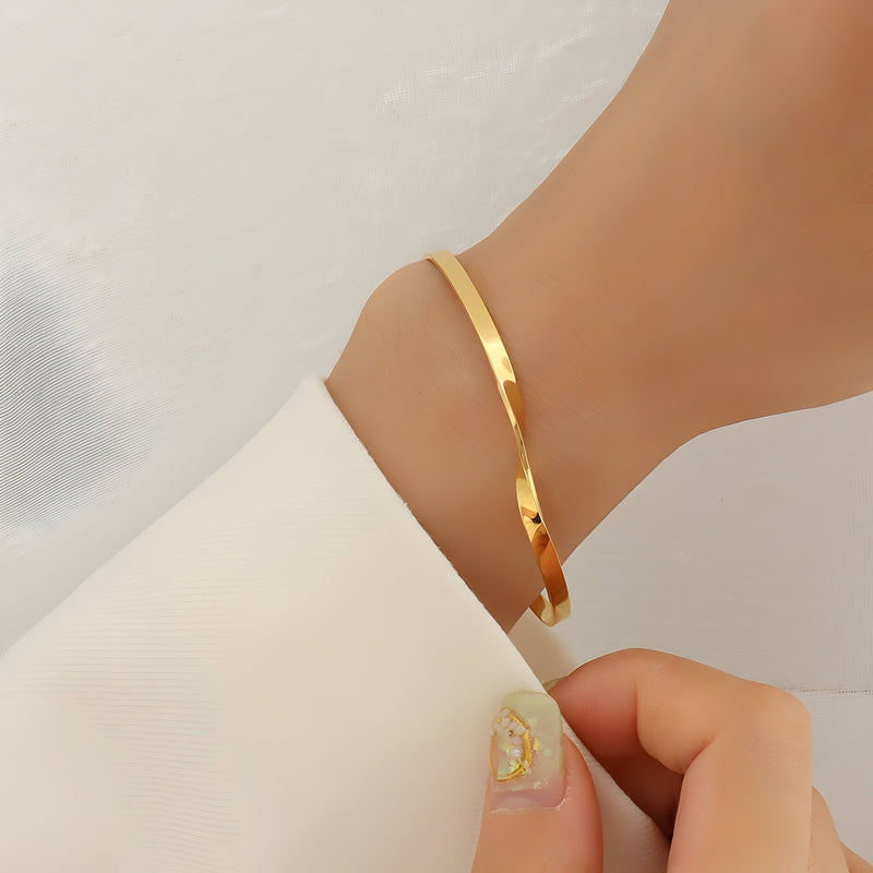 Bracelet fin en titane plaqué or 18 carats avec un design torsadé élégant porté au poignet.