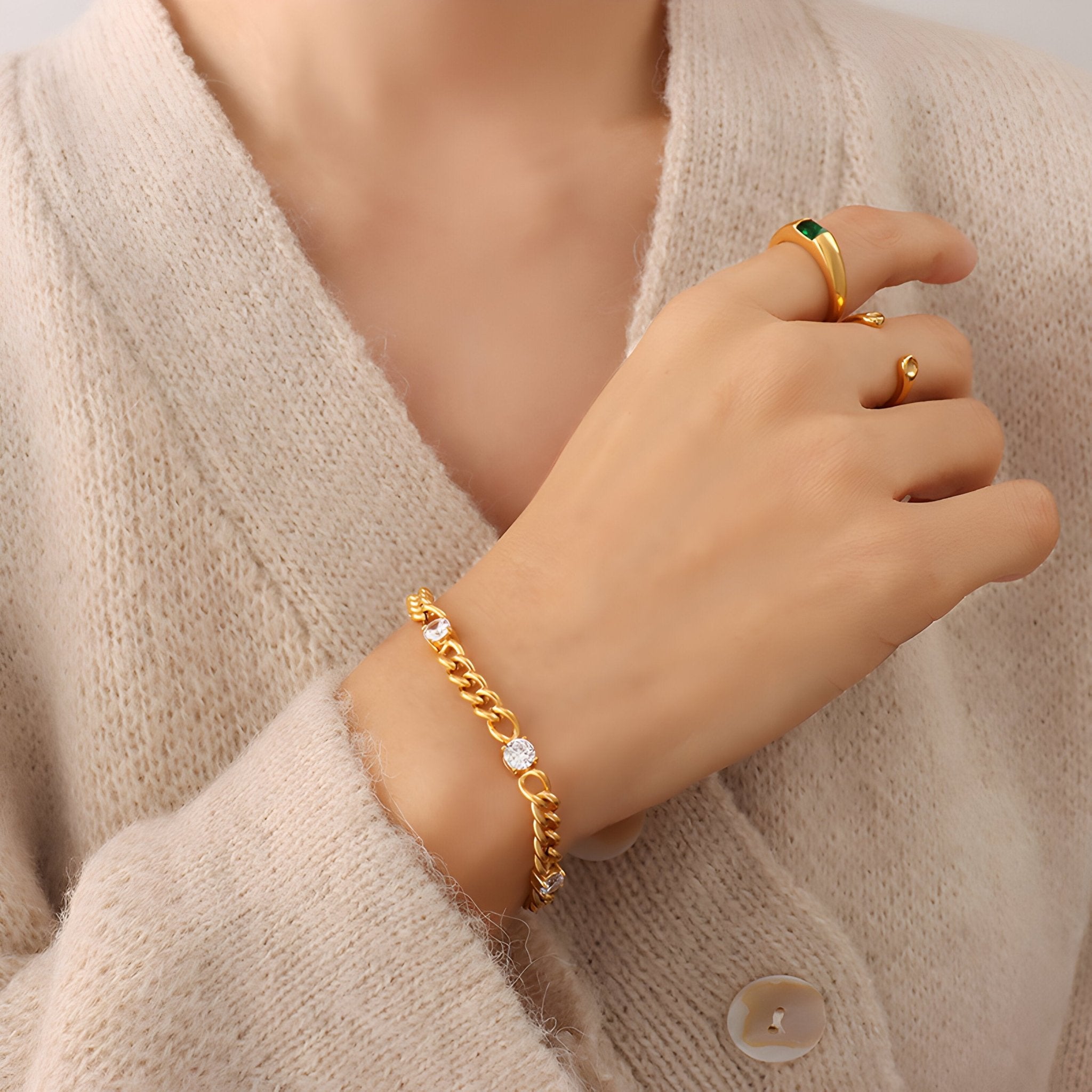 Bracelet doré en titane avec maillons larges et quatre pierres de zircon éclatantes, porté au poignet féminin.