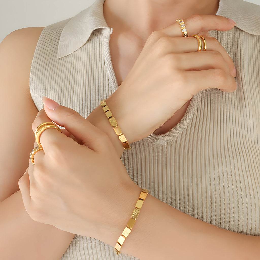 Bracelet en titane plaqué or 18 carats à maillons carrés, style minimaliste, porté avec bagues assorties.