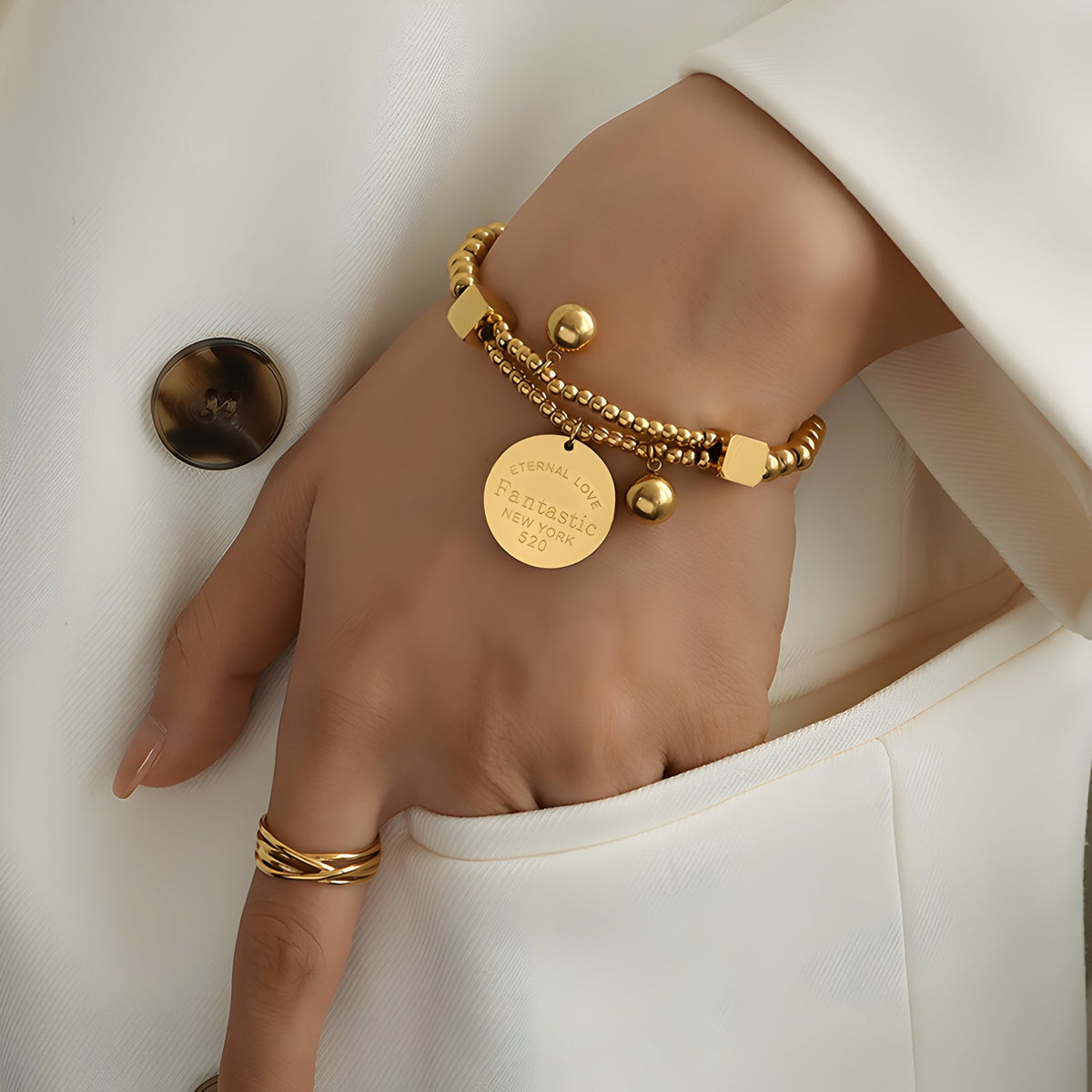 Bracelet en titane plaqué or avec perles dorées et médaillon gravé porté au poignet.