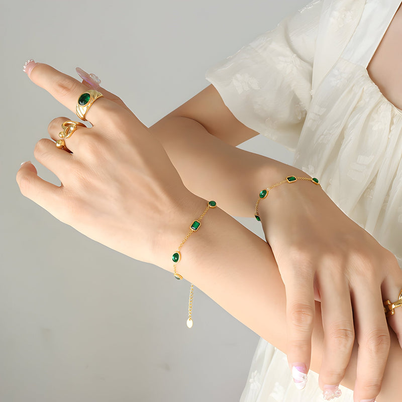 Bracelet en titane plaqué or avec pierres de zircons verts imitation émeraude, style délicat, porté au poignet féminin.