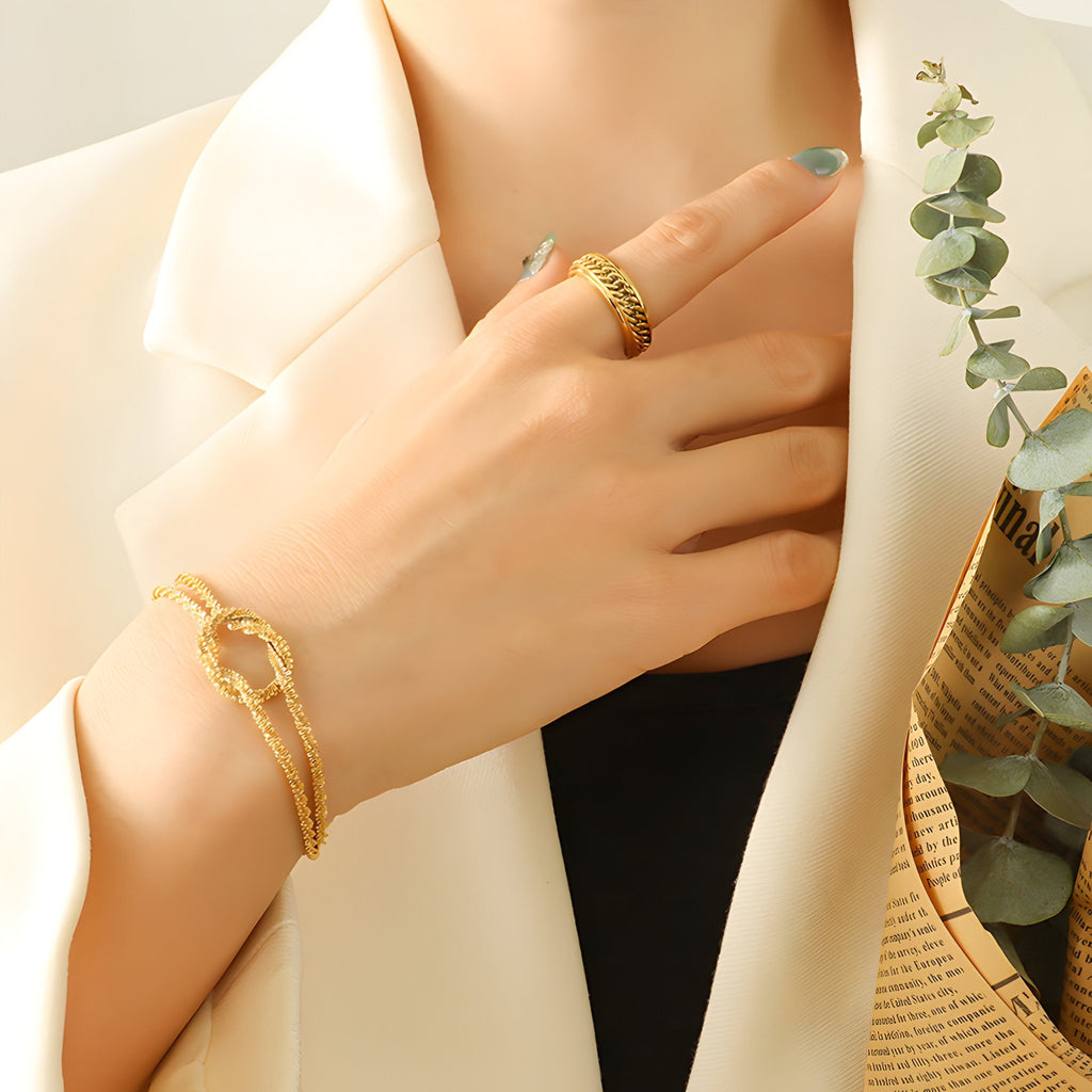 Bracelet en titane plaqué or effet tressé avec fermeture boucle, porté au poignet féminin chic.