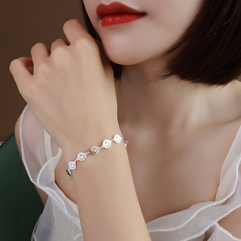 Bracelet en titane plaqué or à motifs smileys stylisés porté au poignet féminin avec peau claire et blouse blanche.