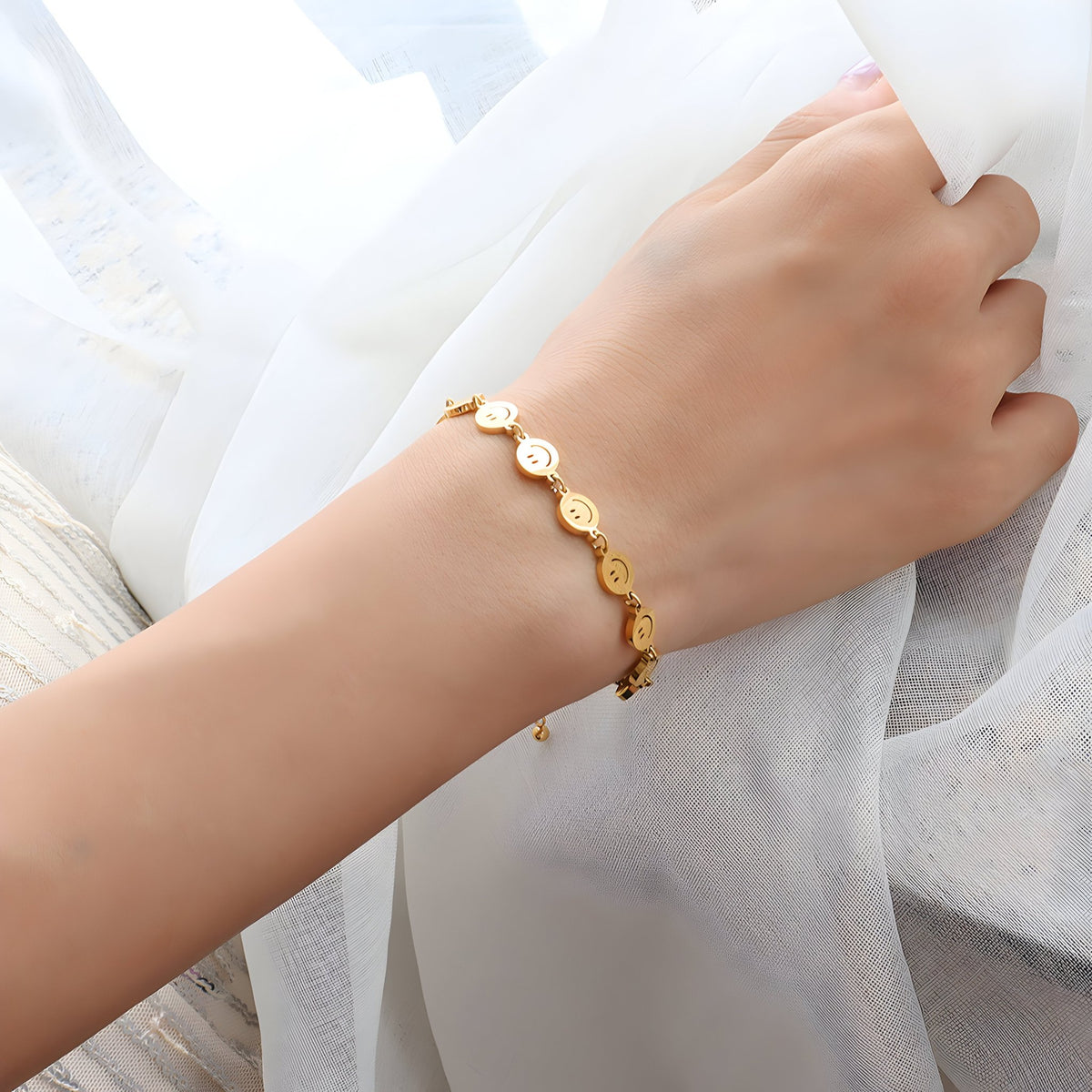 Bracelet fin en titane plaqué or avec motifs smileys ronds, porté au poignet féminin.