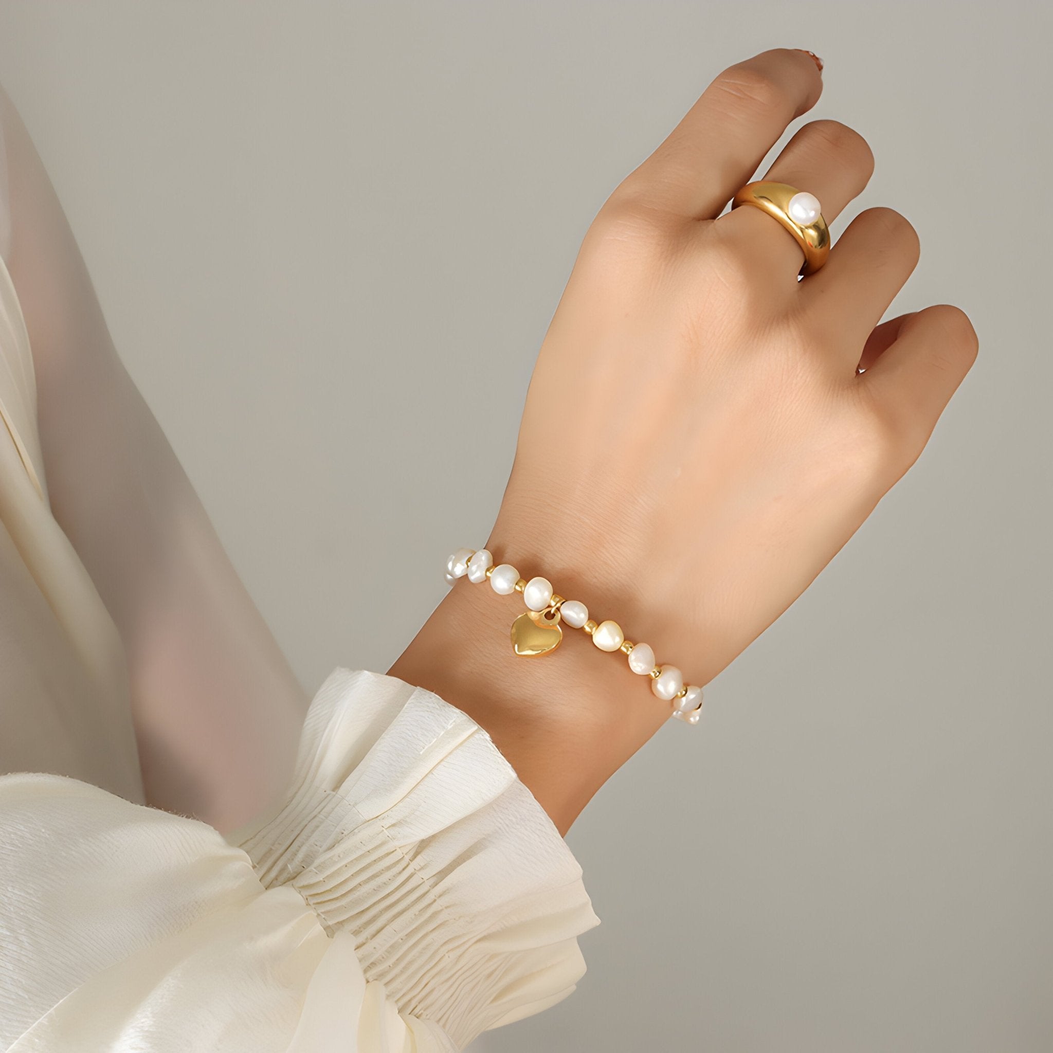 Bracelet perlé en titane plaqué or avec pendentif cœur, style délicat et féminin, porté au poignet.