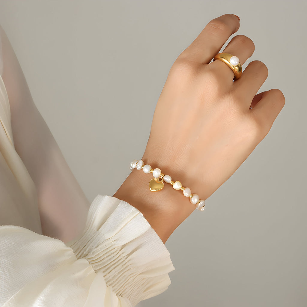 Bracelet perlé en titane plaqué or avec pendentif cœur, style délicat et féminin, porté au poignet.